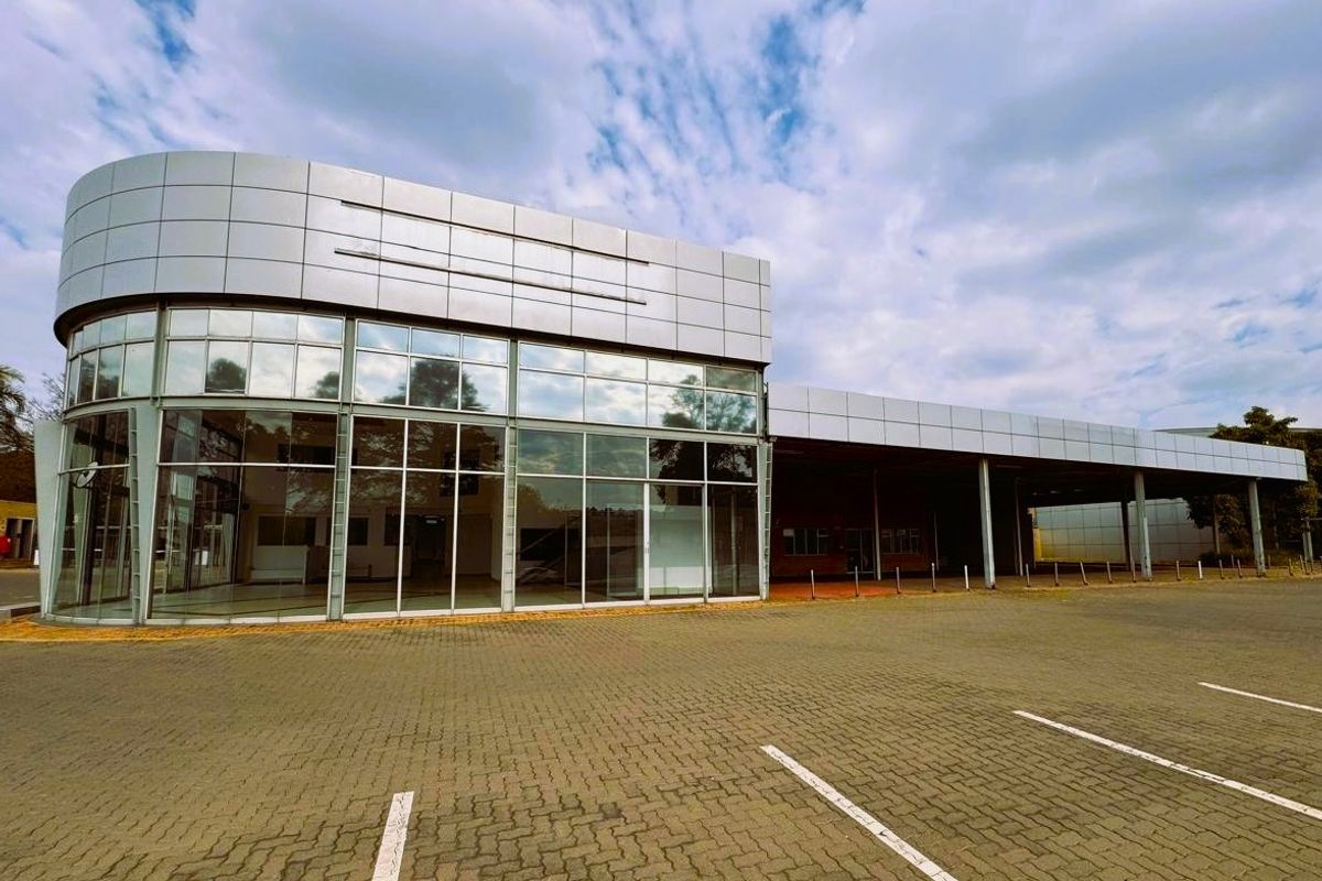 Modern commercial retail building featuring a prominent curved glass facade, metal panel cladding, and an expansive paved parking area with a covered canopy.