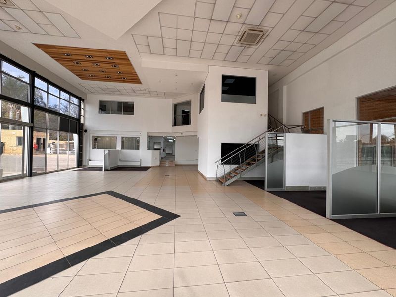 Spacious open-plan retail area featuring high ceilings, large glass windows, tiled flooring, and a central staircase, offering a versatile layout for commercial use.