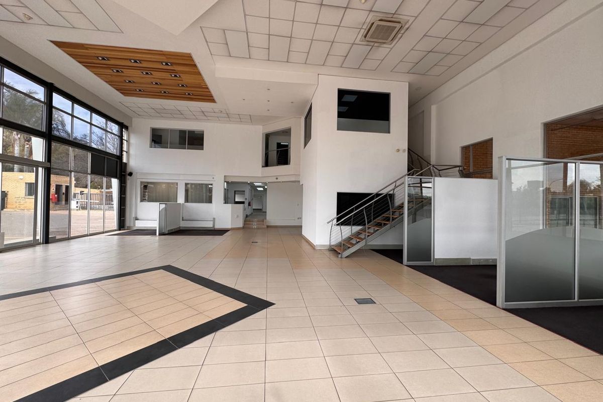Spacious open-plan retail area featuring high ceilings, large glass windows, tiled flooring, and a central staircase, offering a versatile layout for commercial use.