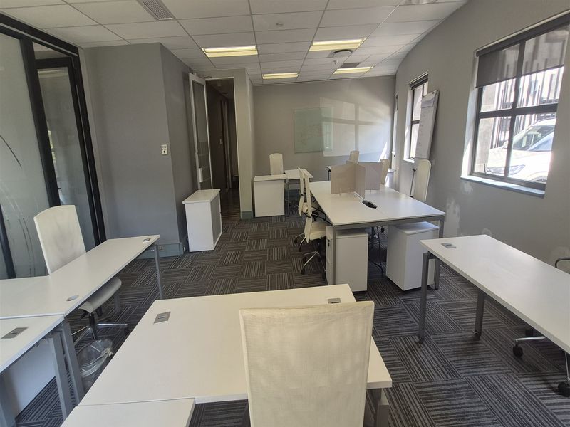 A functional office space featuring carpeted flooring, suspended ceiling with recessed lighting, and a glass partition wall, providing a professional work environment.