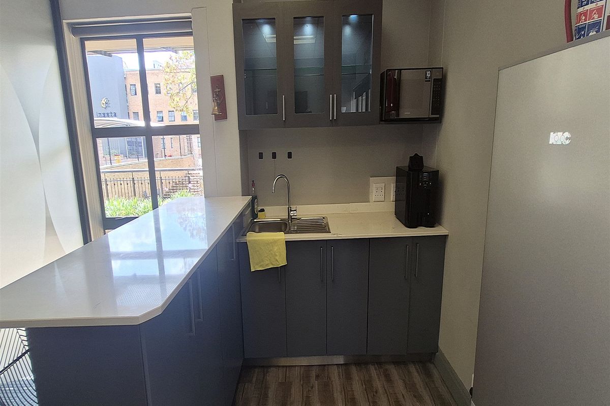 A compact office kitchenette featuring modern grey cabinetry, stone countertops, a stainless steel sink, and integrated microwave, providing a functional break area.