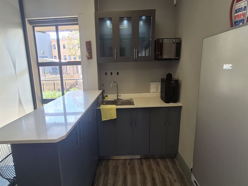 A compact office kitchenette featuring modern grey cabinetry, stone countertops, a stainless steel sink, and integrated microwave, providing a functional break area.