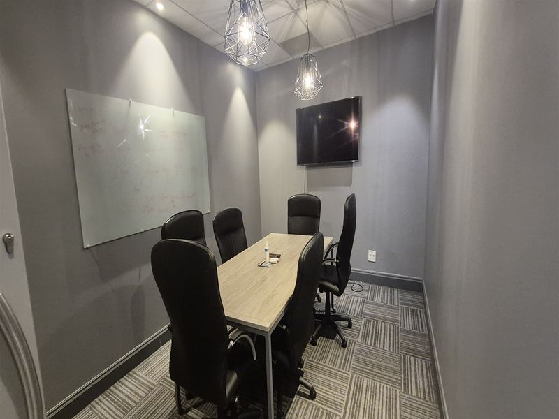 A modern, well-lit office meeting room featuring carpet tiles, a wall-mounted whiteboard, and contemporary pendant lighting.
