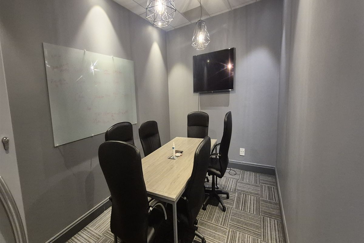 A modern, well-lit office meeting room featuring carpet tiles, a wall-mounted whiteboard, and contemporary pendant lighting.
