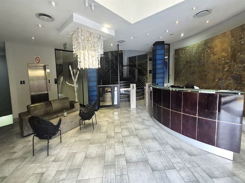 Modern office building reception area featuring a professional reception desk, elevator access, secure turnstile entry, and a grand staircase.