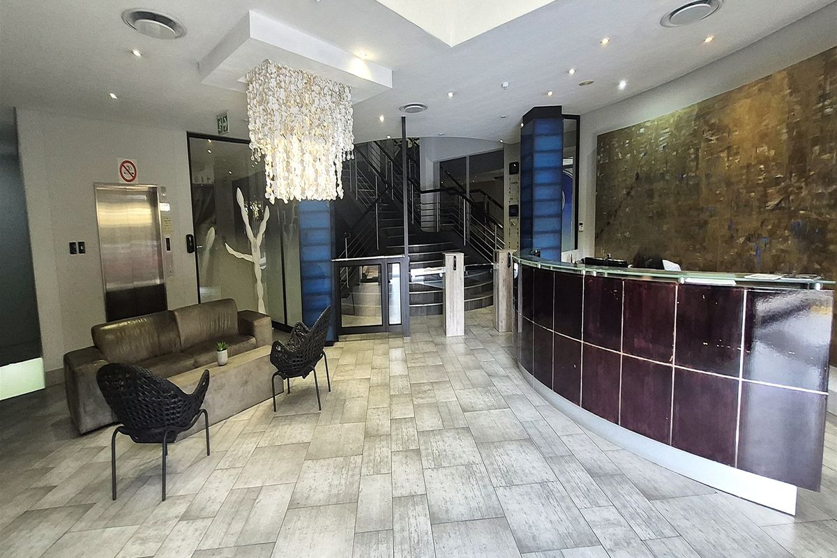 Modern office building reception area featuring a professional reception desk, elevator access, secure turnstile entry, and a grand staircase.