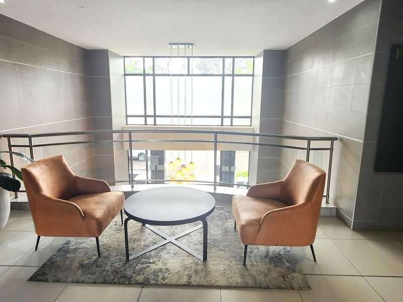 A modern office building landing area featuring tiled flooring, sleek stainless steel balustrades, and a large window providing natural light.