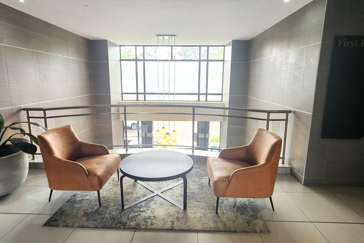 A modern office building landing area featuring tiled flooring, sleek stainless steel balustrades, and a large window providing natural light.