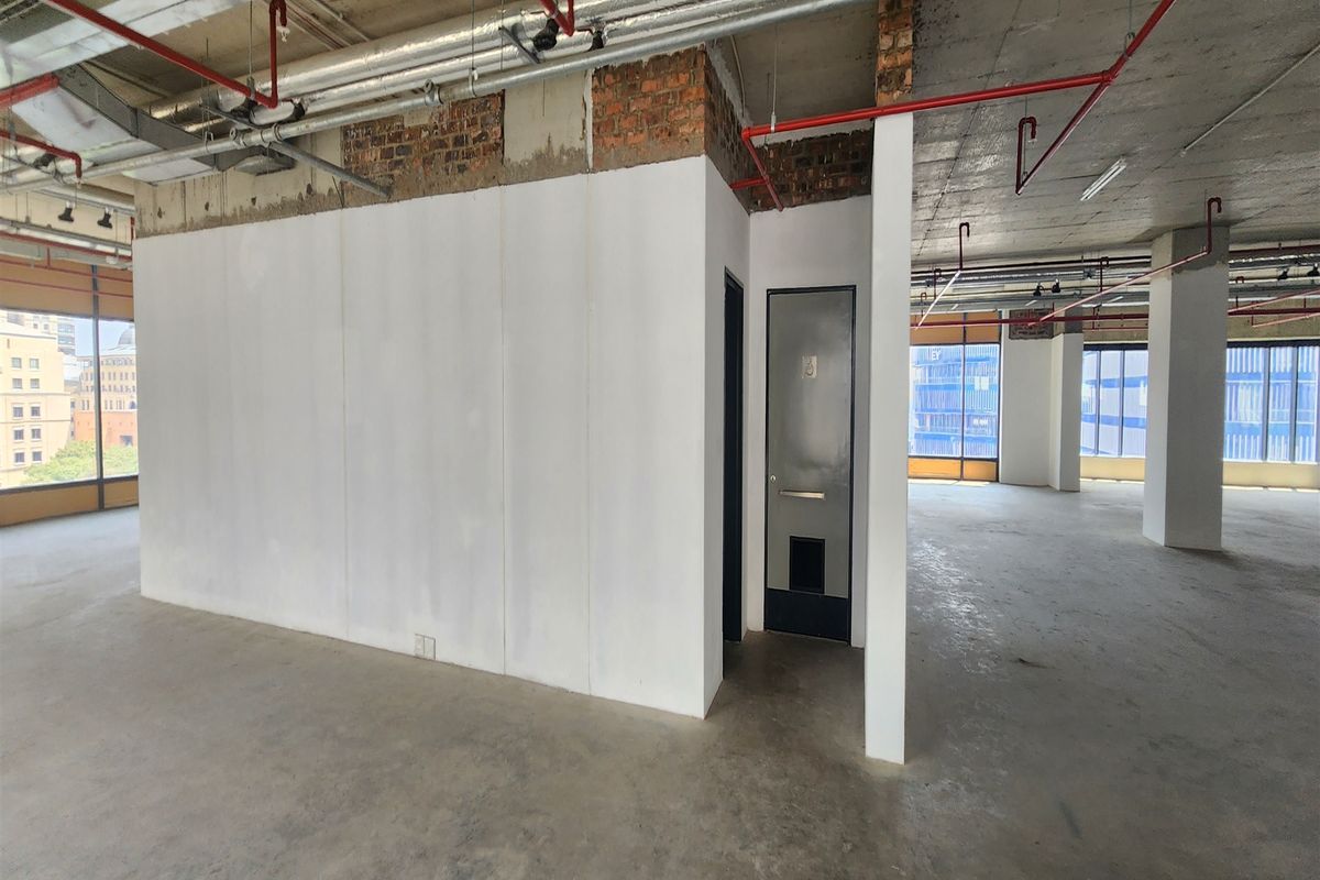 Open-plan office space featuring an industrial aesthetic with exposed ceilings, concrete flooring, and large windows providing ample natural light.