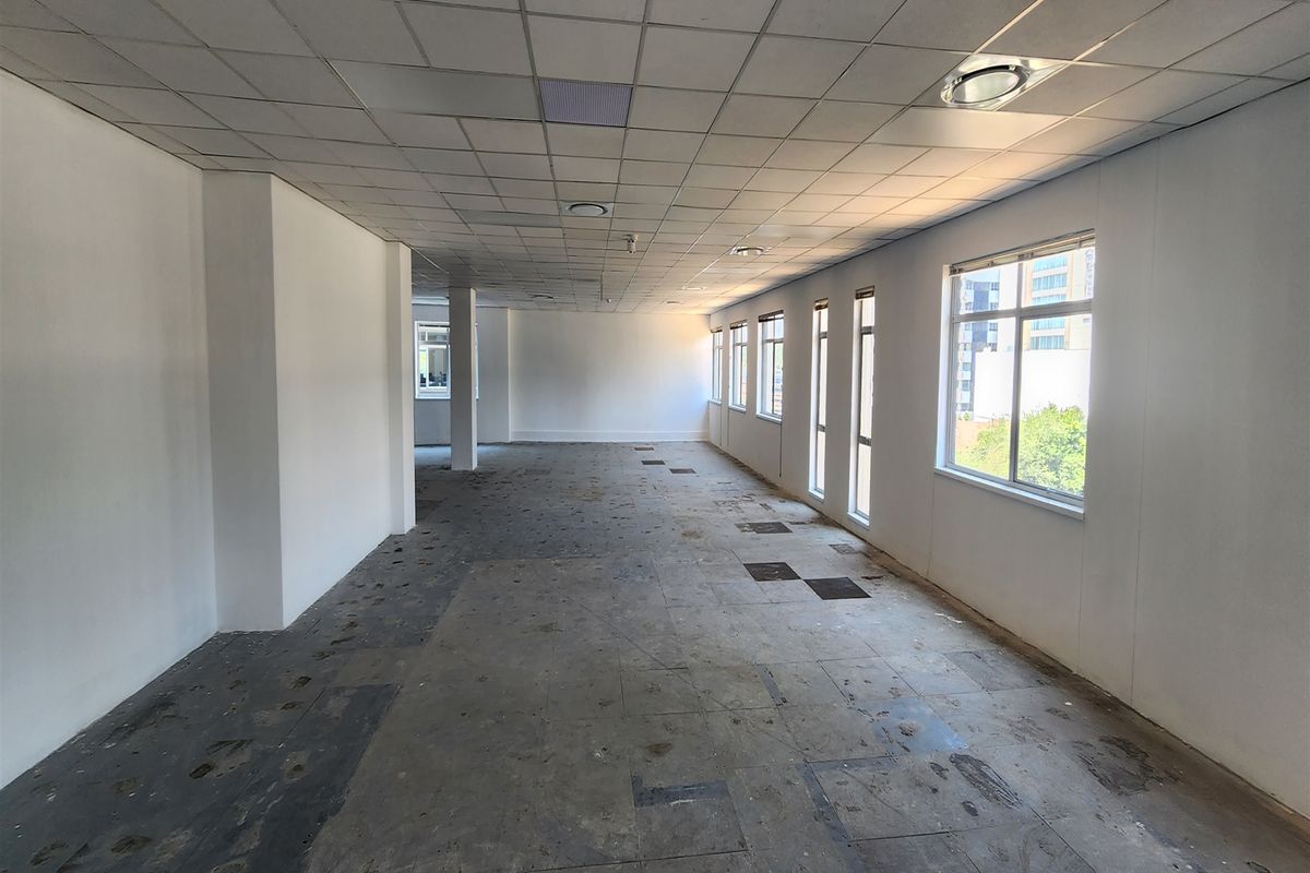 A spacious, vacant open-plan office area featuring a suspended ceiling, recessed lighting, and large windows providing ample natural light.