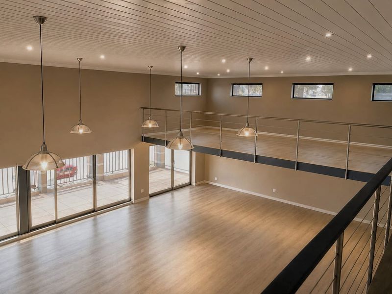Spacious open-plan retail or commercial area featuring a mezzanine level, modern pendant lighting, timber laminate flooring, and large sliding glass doors for natural light.