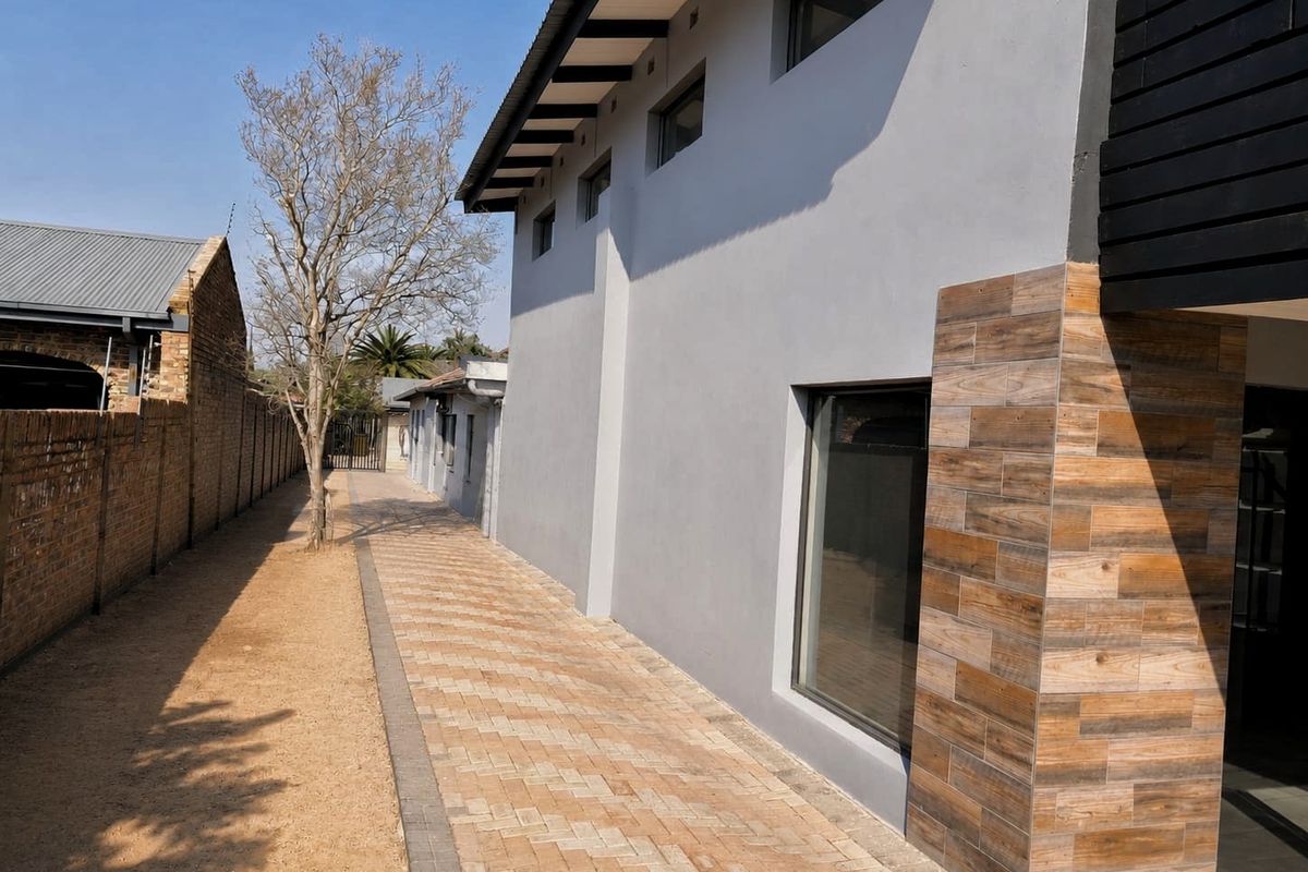 Side view of the property featuring a paved walkway, modern grey exterior walls with wood-look tile accents, and a brick boundary wall.