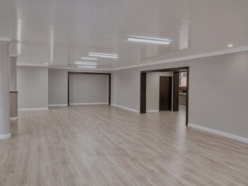 A spacious, open-plan retail area featuring modern laminate flooring, neutral walls, crown molding, and bright overhead lighting, offering a versatile commercial layout.