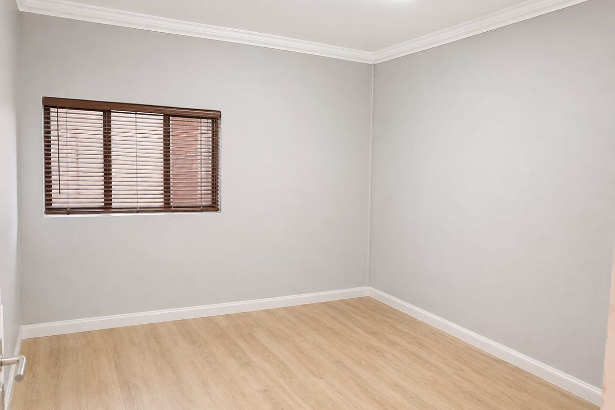 A clean, vacant bedroom featuring light-toned laminate flooring, neutral walls, and fitted venetian blinds, offering a versatile space ready for customization.