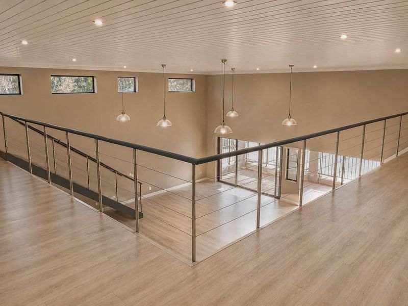 Spacious open-plan mezzanine level featuring modern laminate flooring, stainless steel balustrades, and high-quality pendant lighting with views overlooking the lower level.
