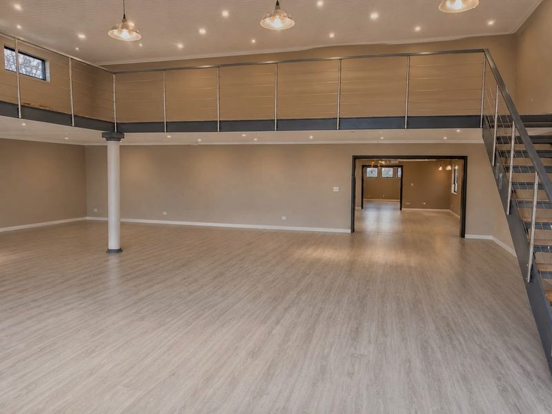 Spacious open-plan retail area featuring a mezzanine level, modern metal staircase, laminate flooring, and contemporary recessed and pendant lighting throughout.