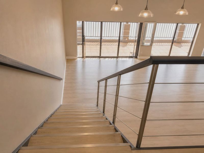 A bright, modern staircase leading down to an open-plan living area with large sliding glass doors opening onto a balcony.