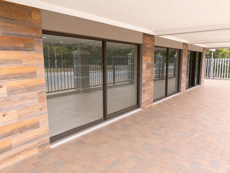 A modern covered patio area featuring wood-look tile wall cladding, paved flooring, and large sliding glass doors providing access to the interior.
