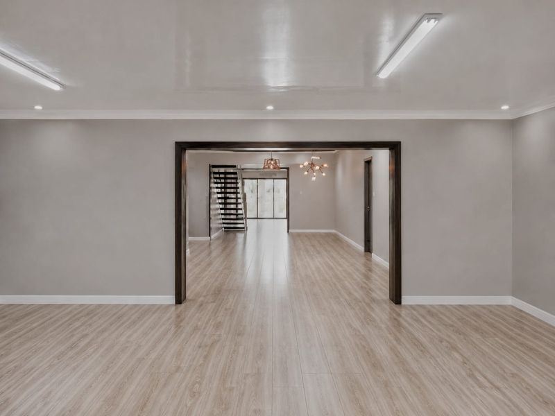 Spacious open-plan retail area featuring light wood-look laminate flooring, neutral walls, and a connecting staircase leading to an additional level.