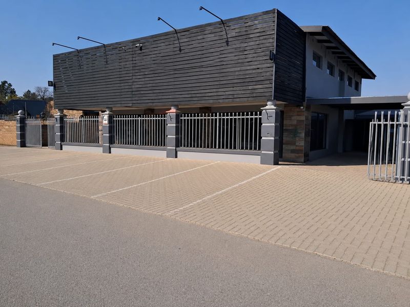 Front exterior view of a commercial property featuring a paved parking area, secure metal fencing, and modern timber-clad facade elements.