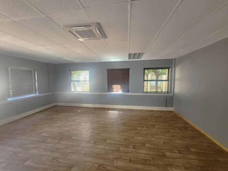 A spacious, empty office area featuring vinyl flooring, a suspended ceiling with integrated lighting, air conditioning, and multiple windows with fitted blinds.