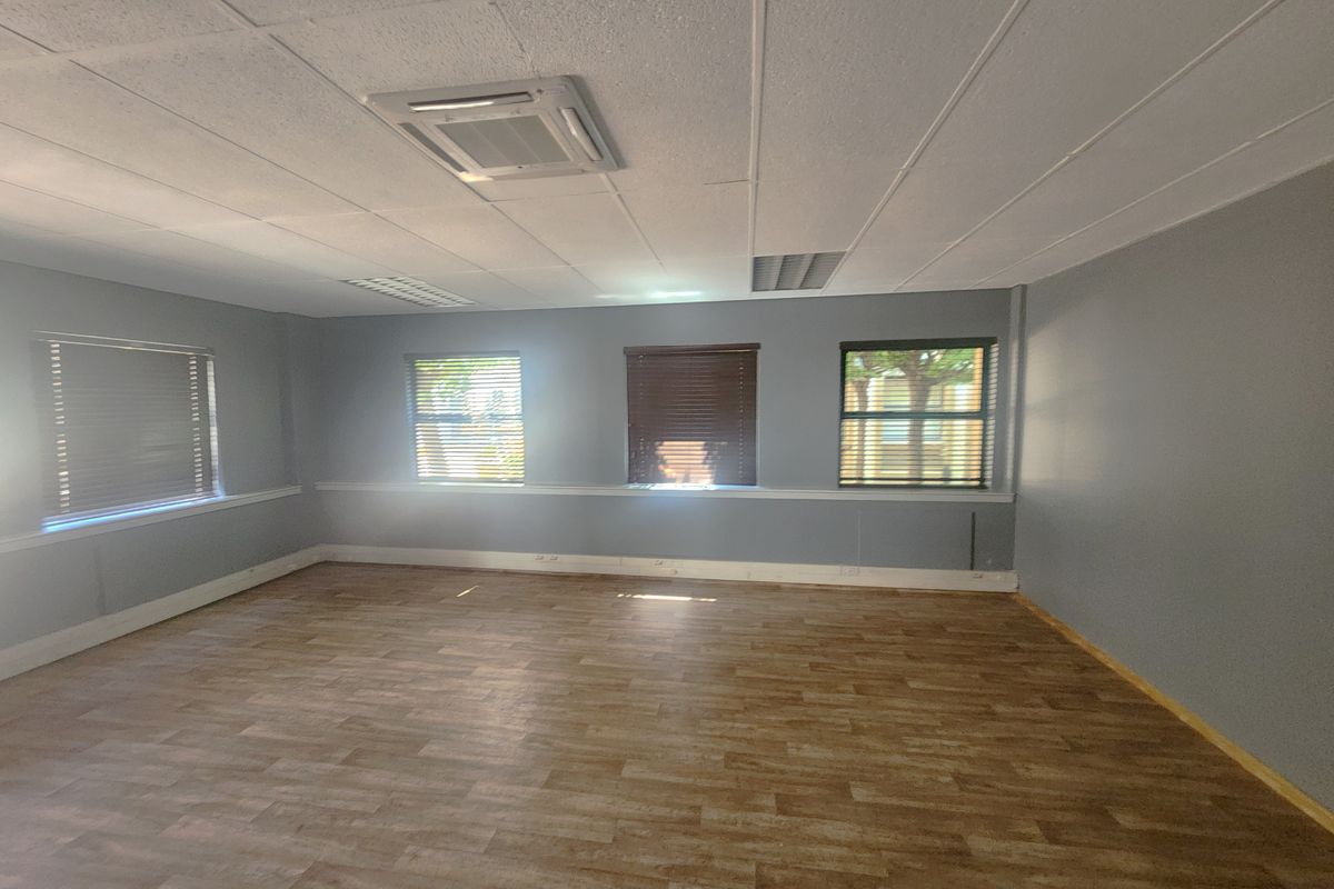 A spacious, empty office area featuring vinyl flooring, a suspended ceiling with integrated lighting, air conditioning, and multiple windows with fitted blinds.