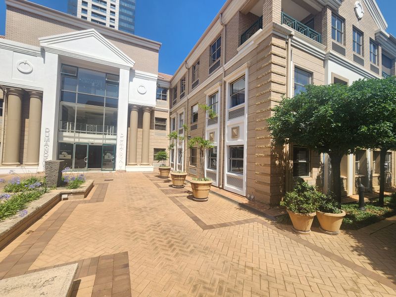 A professional office building exterior featuring a paved courtyard, classical architectural columns, and a modern glass entrance facade.