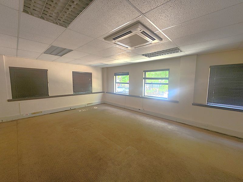 An empty office space featuring a suspended ceiling, recessed lighting, cassette air conditioning, and carpet flooring with multiple windows.
