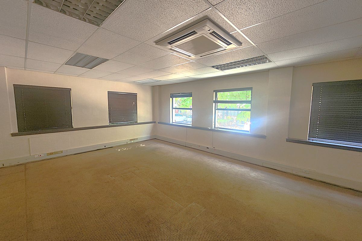 An empty office space featuring a suspended ceiling, recessed lighting, cassette air conditioning, and carpet flooring with multiple windows.