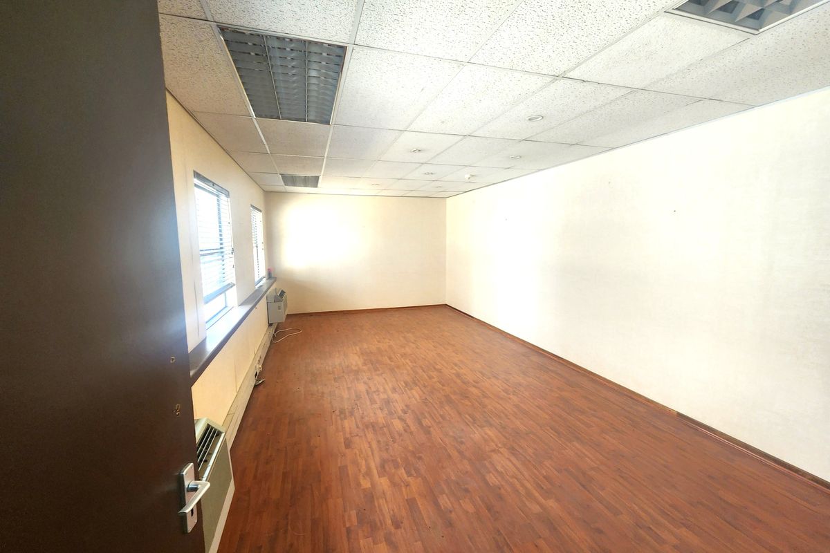 An empty office space featuring laminate flooring, a suspended ceiling with recessed lighting, and a wall-mounted air conditioning unit.