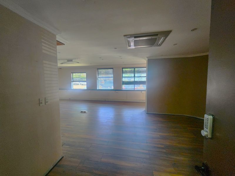 An open-plan office space featuring laminate flooring, recessed ceiling air conditioning, and large windows with venetian blinds, providing a bright and functional workspace.