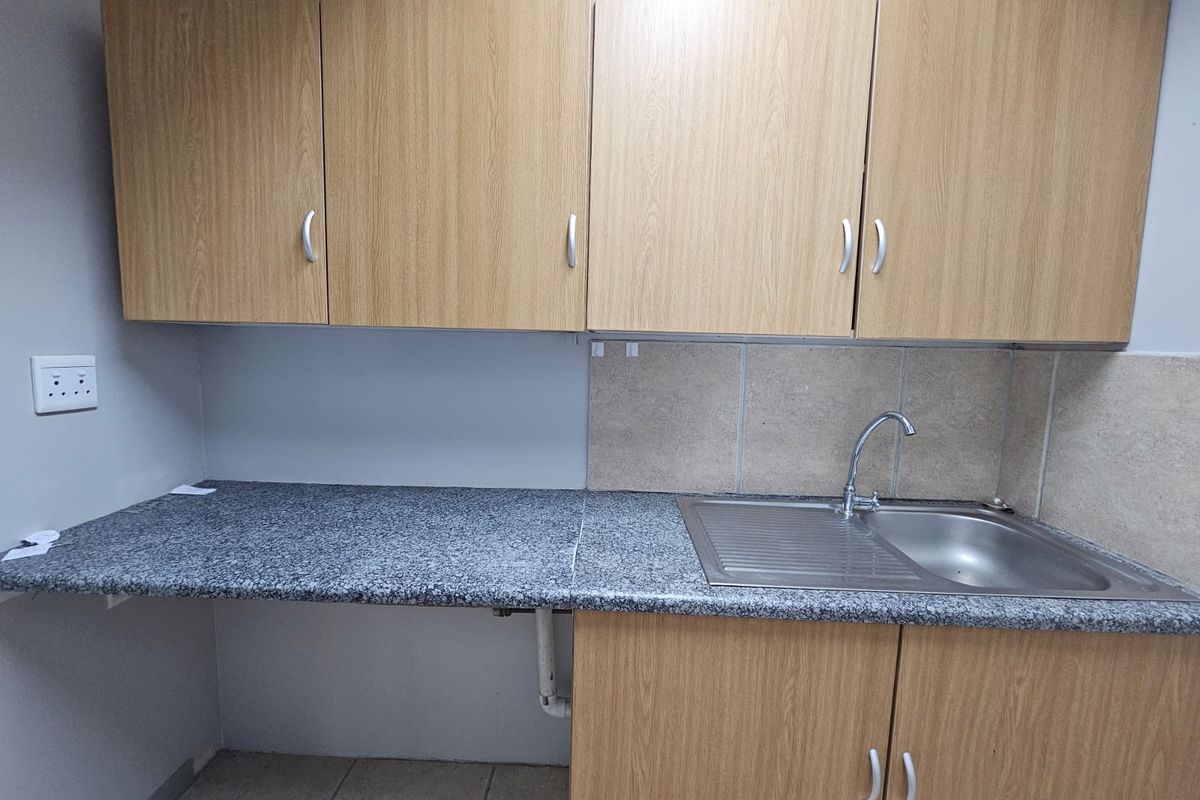 A functional kitchen area featuring laminate cabinetry, granite countertops, and a stainless steel sink with a tiled splashback.