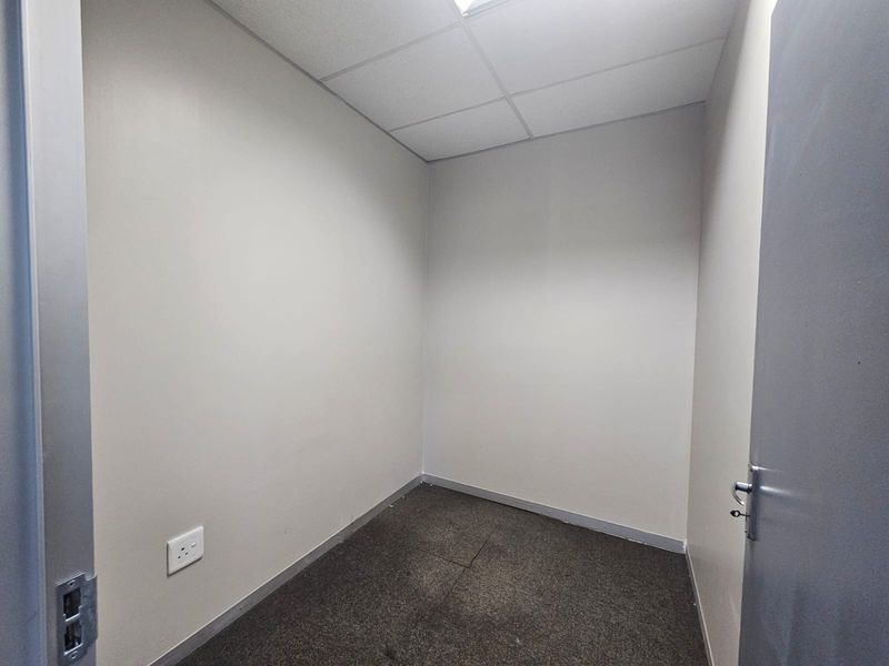A compact, empty office space featuring neutral walls, a suspended ceiling, and carpeted flooring, suitable for a private workspace or storage area.