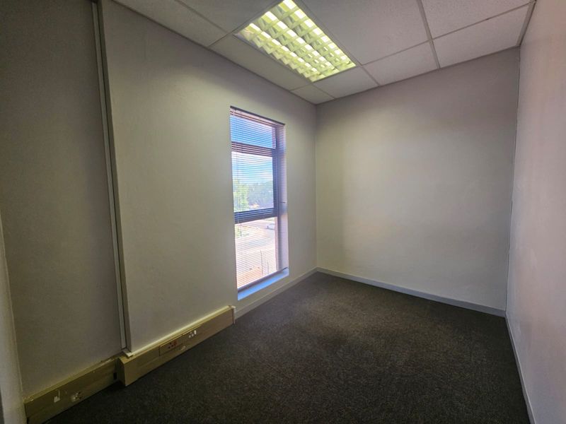 A vacant office space featuring a suspended ceiling with recessed lighting, carpeted flooring, and a window with fitted venetian blinds.