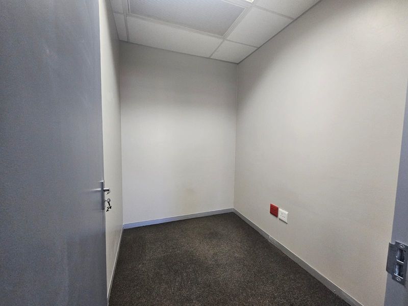 A small, empty office space featuring neutral walls, carpeted flooring, and a suspended ceiling with integrated electrical and data connectivity.