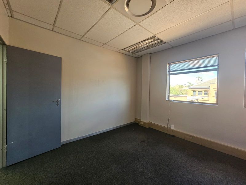A vacant office space featuring a suspended ceiling, recessed lighting, carpeted flooring, and a window providing natural light.