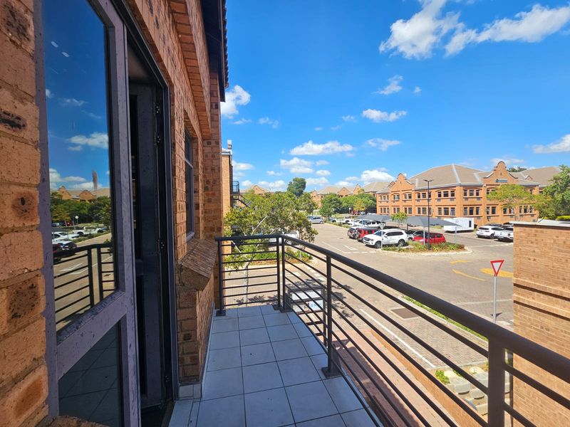 A clean, tiled balcony with a metal balustrade, offering an elevated view of the surrounding business park and parking area.