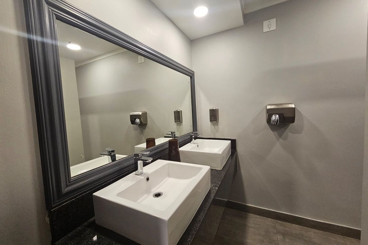 Modern commercial bathroom featuring a double vessel sink vanity with granite countertop, large framed mirror, and wall-mounted fixtures.