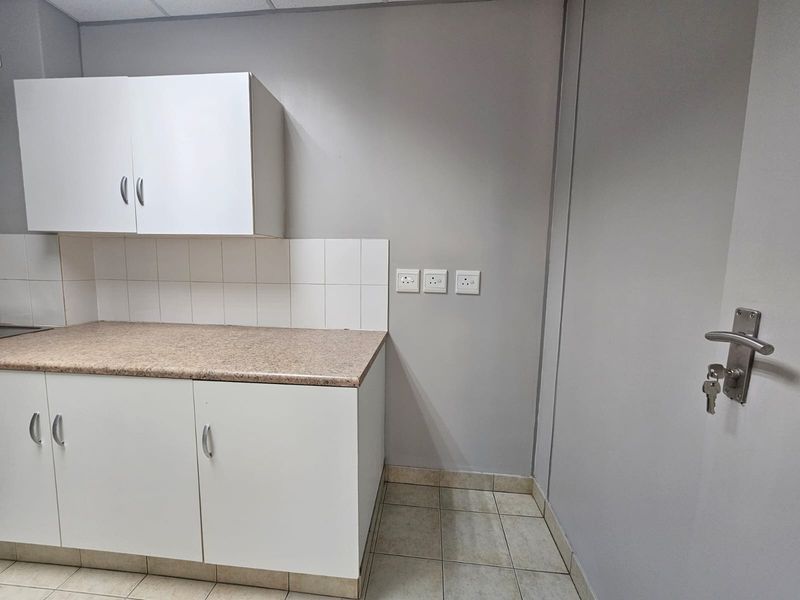A functional kitchenette area featuring built-in white cabinetry, laminate countertops, tiled splashback, and ceramic floor tiles.
