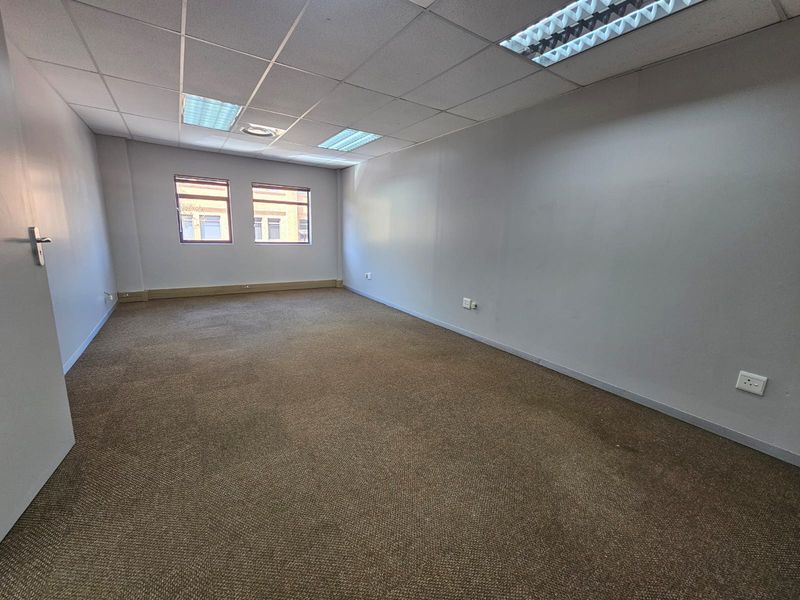 An empty, open-plan office space featuring a suspended ceiling with recessed lighting, carpeted flooring, and neutral wall finishes.