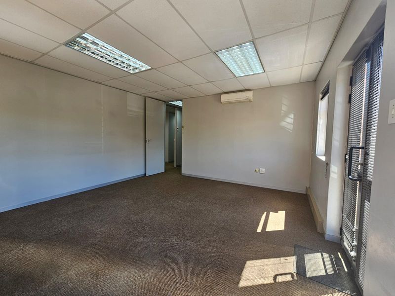 A vacant office space featuring a suspended ceiling with recessed lighting, wall-mounted air conditioning, and carpeted flooring.
