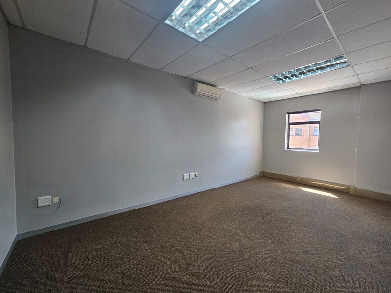 A vacant, well-lit office space featuring a suspended ceiling, recessed lighting, split-system air conditioning, and carpeted flooring.