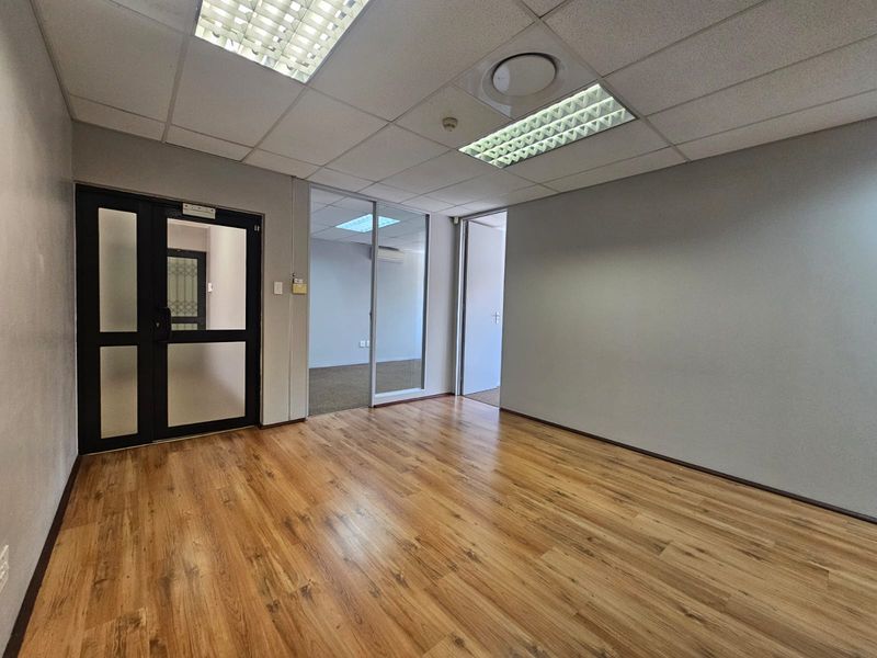 A vacant office space featuring laminate flooring, a suspended ceiling with recessed lighting, and a glass partition wall providing a professional, open feel.