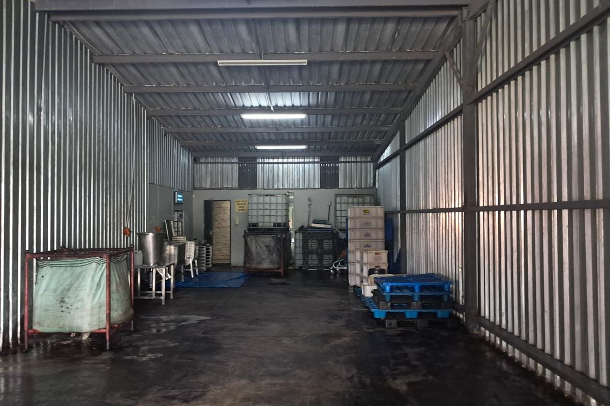 Industrial utility space featuring corrugated metal walls, high-clearance ceiling with fluorescent lighting, and durable concrete flooring suitable for storage or processing operations.