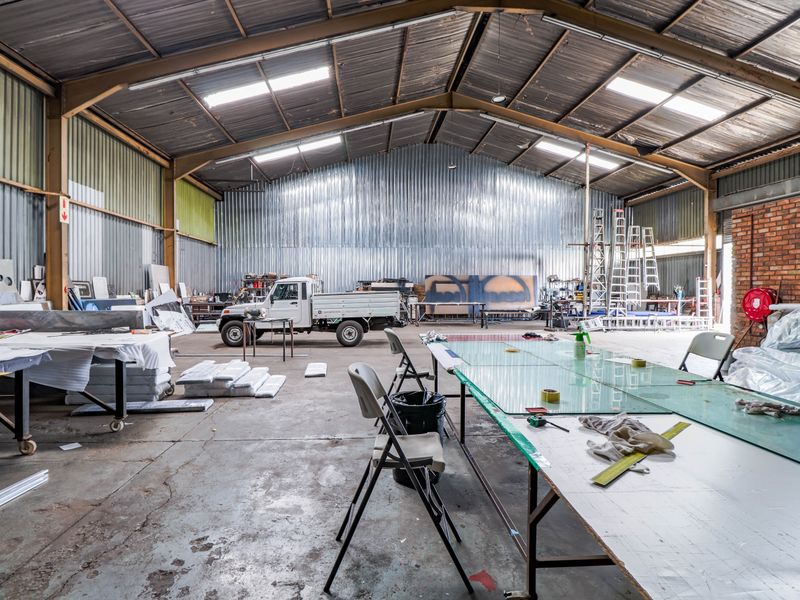 Spacious industrial warehouse featuring high-pitched corrugated metal roofing, exposed steel trusses, concrete flooring, and large open-plan workspace suitable for manufacturing or storage operations.