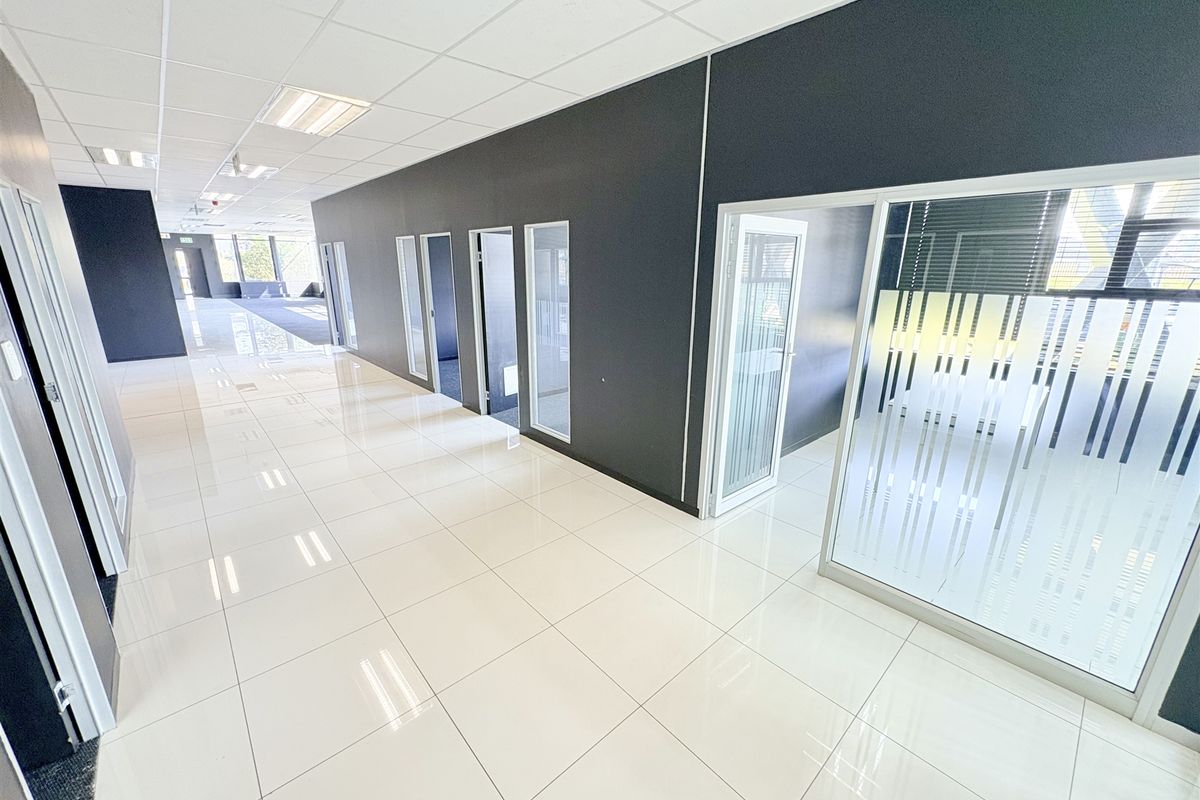 Modern open-plan office space featuring polished tiled flooring, suspended ceilings with recessed lighting, and contemporary glass partition walls for private meeting areas.