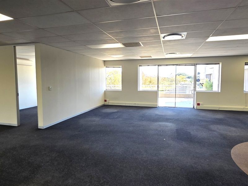 Spacious open-plan office area featuring a suspended ceiling, recessed lighting, glass partitions, and direct access to an outdoor balcony through sliding glass doors.