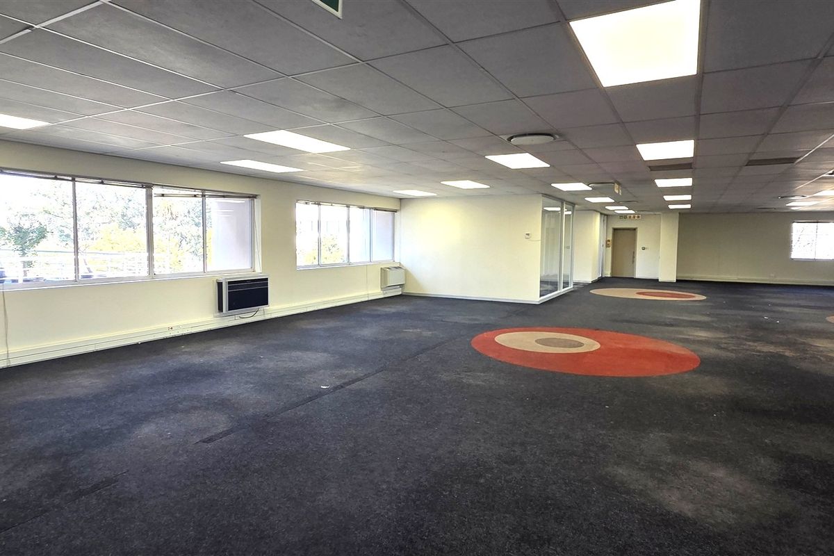 Spacious open-plan office area featuring suspended ceilings, recessed lighting, wall-mounted air conditioning units, and large windows providing ample natural light.