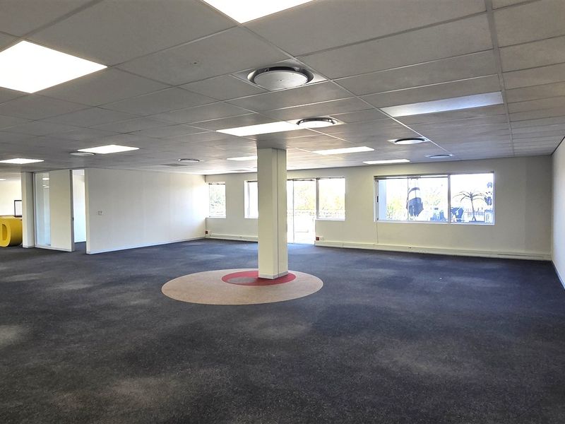 Spacious open-plan office area featuring suspended ceilings, recessed lighting, glass partitions, and a central support column, offering a versatile workspace layout.