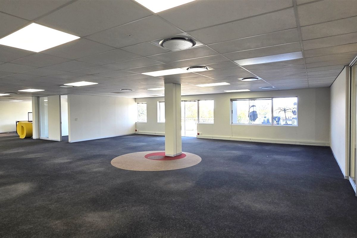 Spacious open-plan office area featuring suspended ceilings, recessed lighting, glass partitions, and a central support column, offering a versatile workspace layout.